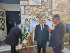 Scene before funeral the ceremony. 2 men in front of a church with flowers on the wall and a woman fixing a display.