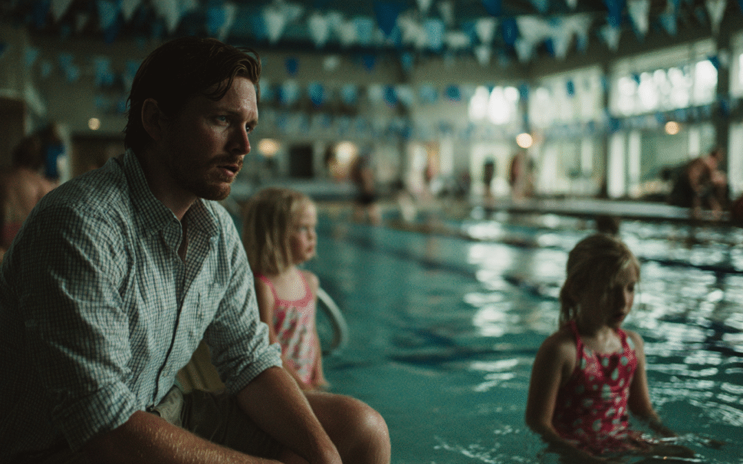 business man dad sitting at edge of pool with two young daughters who are not participating in swim lesson and missing out.