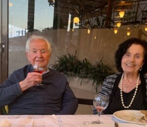 Older Gentleman drinking a small glass of village wine next to his wife.