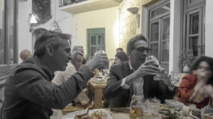 couple of men in black and white drinking wine inside a Greek taverna cafe in colour