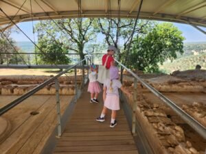 woman and 2 children on a wooden bridge looking below as the ruins of Nestor Palace in Pylos Greece